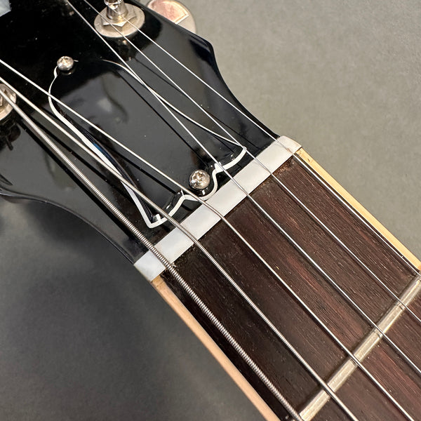 Close-up of electric guitar headstock and fretboard with metal strings and black tuning pegs on gray background