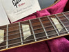 Close-up of Gibson guitar rosewood fretboard with mother-of-pearl block inlays and metal frets inside a pink plush-lined guitar case showing Gibson Custom booklet