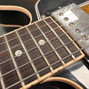 Close-up of electric guitar neck showing rosewood fretboard, metal frets, pearl dot inlays, and vintage metal humbucker pickup on black guitar body