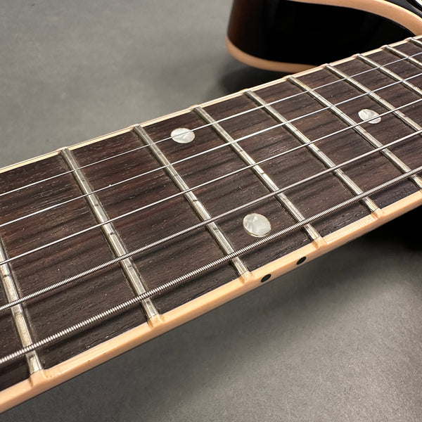 Close-up of electric guitar fretboard with mother-of-pearl dot inlays and steel strings on dark wood fingerboard