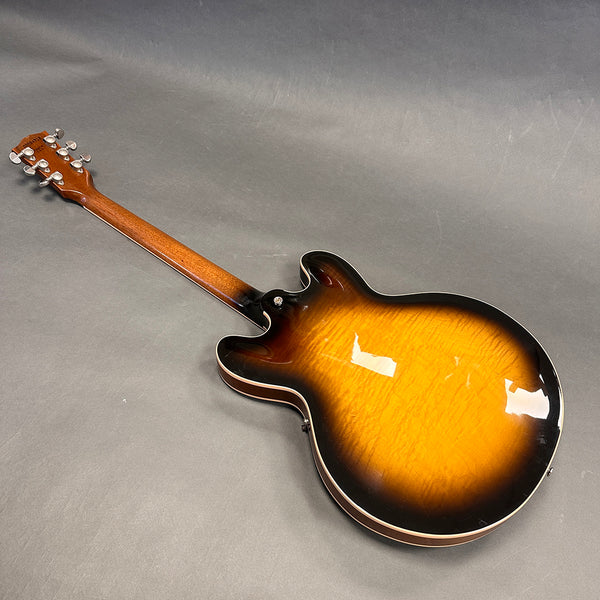 Electric semi-hollow body guitar with sunburst finish viewed from the back showing wood grain and neck with tuning pegs