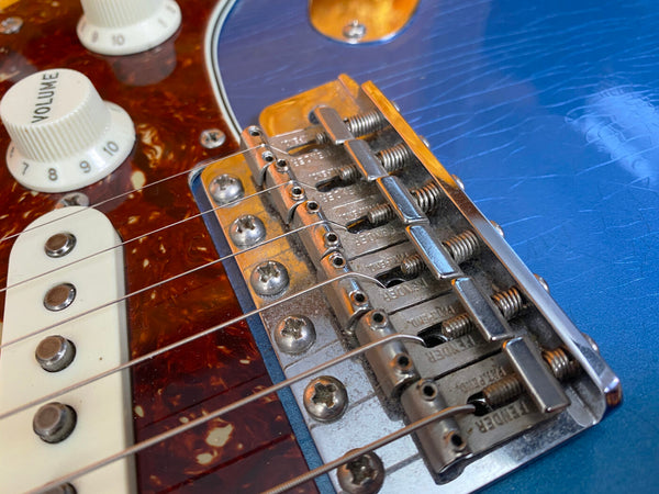 Close-up of vintage Fender electric guitar bridge, blue body, tortoiseshell pickguard, and volume control knob