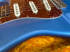 Close-up of blue electric guitar body with tortoiseshell pickguard and white single-coil pickups on orange plush guitar case interior