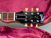 Close-up of Gibson Les Paul Model guitar headstock with tuning pegs and strings on pink velvet-lined guitar case interior