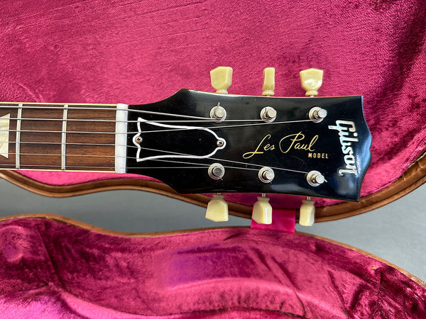 Close-up of Gibson Les Paul Model guitar headstock with tuning pegs and strings on pink velvet-lined guitar case interior
