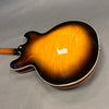Back view of a sunburst finish semi-hollow electric guitar with a flamed maple top and cream binding on a gray background