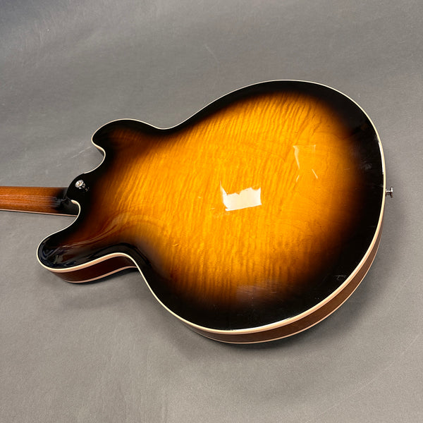 Back view of a sunburst finish semi-hollow electric guitar with a flamed maple top and cream binding on a gray background