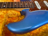 Close-up of blue electric guitar body with tortoiseshell pickguard and white single-coil pickups on yellow plush case lining