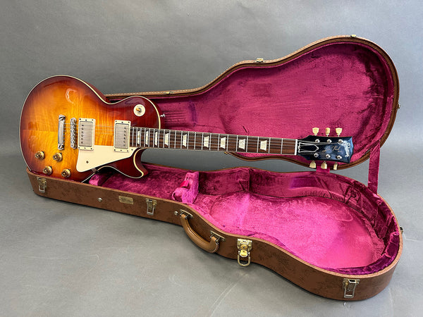 Vintage sunburst Les Paul electric guitar in open brown hard shell case with pink velvet lining on gray background