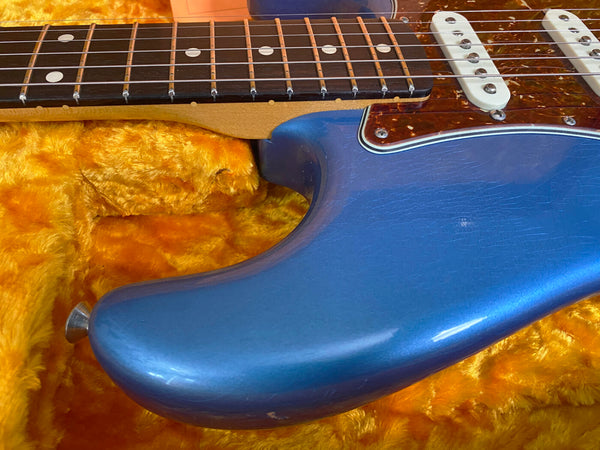 Close-up of blue electric guitar body with tortoiseshell pickguard and white single-coil pickups on yellow plush case lining