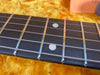 Close-up of guitar fretboard with metal frets and dot inlays on dark wood, steel strings visible, yellow guitar case lining background