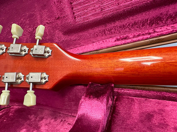 Close-up of classic vintage guitar neck and tuning pegs with cream tuning keys resting in pink velvet guitar case interior