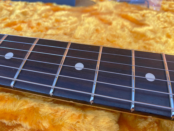 Close-up of guitar fretboard with dot inlays and metal strings on plush yellow case lining