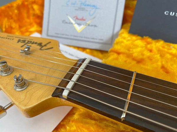 Close-up of Fender Custom Shop guitar headstock and fretboard on yellow plush case lining with Fender Custom Shop tag in background
