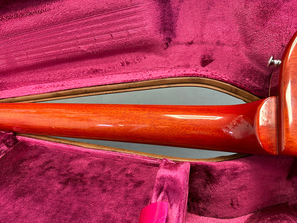 Close-up of polished mahogany guitar neck inside plush pink velvet guitar case