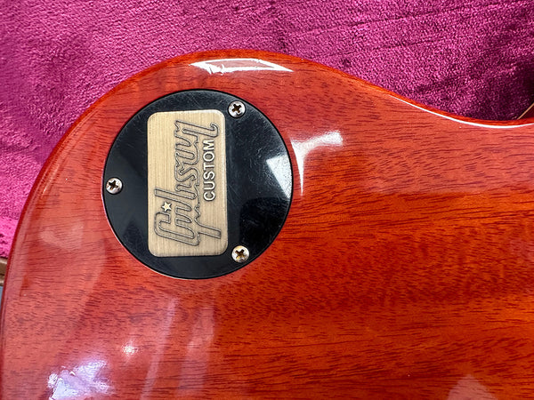 Close-up of Gibson Custom electric guitar back plate on cherry wood finish guitar body with pink fabric background