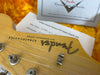 Close-up of Fender Stratocaster guitar headstock with tuning pegs and Coffee House Guitars pre-sales check list in the background