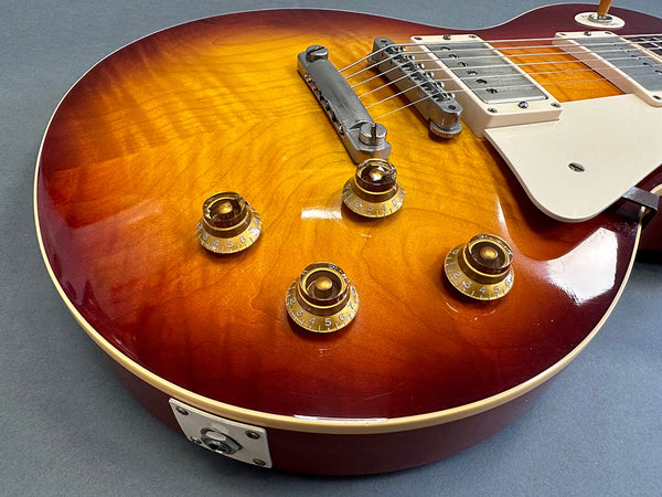 Close-up of sunburst electric guitar body showing control knobs, bridge, pickups, and cream pickguard on blue-gray background