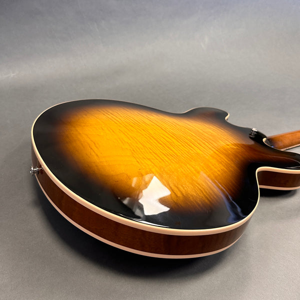 Close-up of the back of a sunburst finished hollow body electric guitar with a gloss finish and cream binding against a gray background