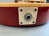 Close-up of vintage electric guitar output jack plate with visible crack on cream-colored plastic mounting plate and red guitar body.