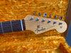 Close-up of Fender Stratocaster guitar headstock with chrome tuning pegs and rosewood fretboard on yellow plush guitar case interior