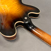 Close-up of sunburst finish hollow body electric guitar back and neck joint with cream binding and strap button on gray background