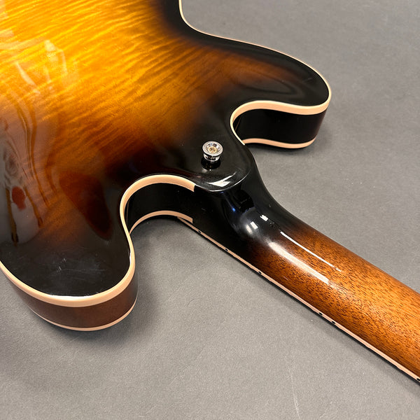 Close-up of sunburst finish hollow body electric guitar back and neck joint with cream binding and strap button on gray background