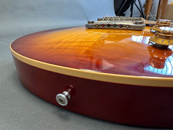 Close-up of sunburst electric guitar body showing bridge, control knobs, and strap button on reddish-brown finish with cream binding.