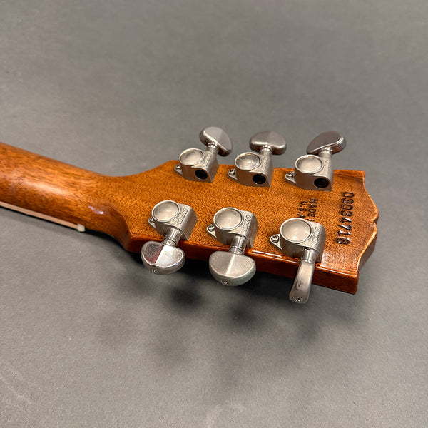 Close-up view of guitar headstock with six chrome tuning pegs, stamped with "Made in USA" and a serial number, showing wood grain finish on the neck.