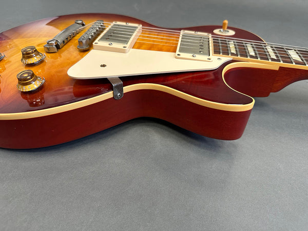Close-up view of sunburst electric guitar body with cream pickguard, dual humbucker pickups, and amber control knobs on gray background