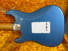 Blue Fender Stratocaster electric guitar body back with white tremolo cavity cover and chrome neck plate on orange vintage plush case interior