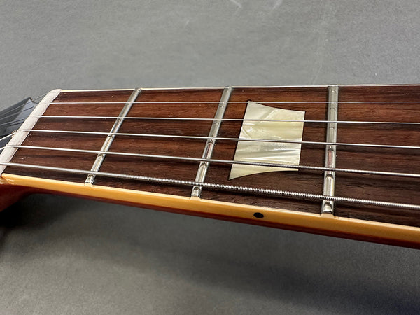 Close-up of guitar neck showing rosewood fretboard with pearl trapezoid inlay and metal frets with steel guitar strings on gray background