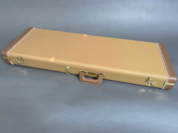 Hard shell tan guitar case with brown leather handle and brass latches on gray background