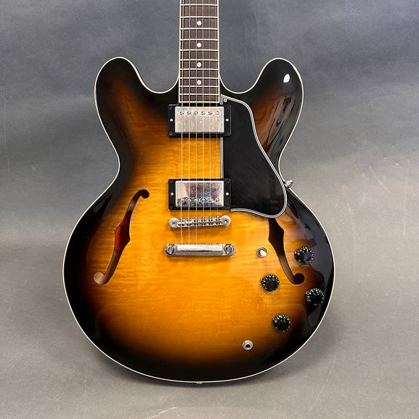 Semi-hollow body electric guitar with sunburst finish, dual humbucker pickups, black pickguard, and four control knobs on gray background