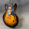 Semi-hollow electric guitar with sunburst finish, dual humbucker pickups, black pickguard, and four control knobs on gray background