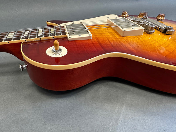 Close-up of cherry sunburst electric guitar body with cream pickups, chrome bridge, and vintage toggle switch on gray surface