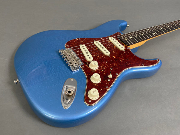Blue electric guitar with tortoise shell pickguard and three single-coil pickups on gray background