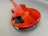 Back view of a glossy red electric guitar body with black control cavity cover and strap button on gray background
