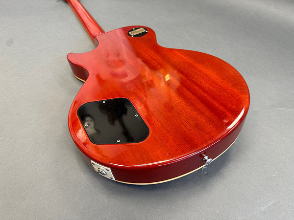 Back view of a glossy red electric guitar body with black control cavity cover and strap button on gray background