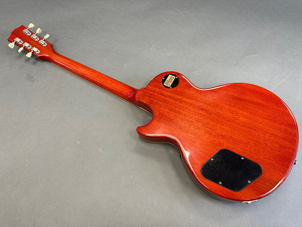 Back view of cherry red electric guitar with mahogany neck and black control cavity cover on gray background