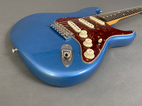 Electric guitar with blue cracked finish, tortoiseshell pickguard, three single-coil pickups, and cream control knobs on gray background