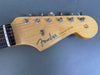 Close-up of Fender Stratocaster guitar headstock with six tuning pegs, natural wood finish, and "Original Contour Body" text on gray background
