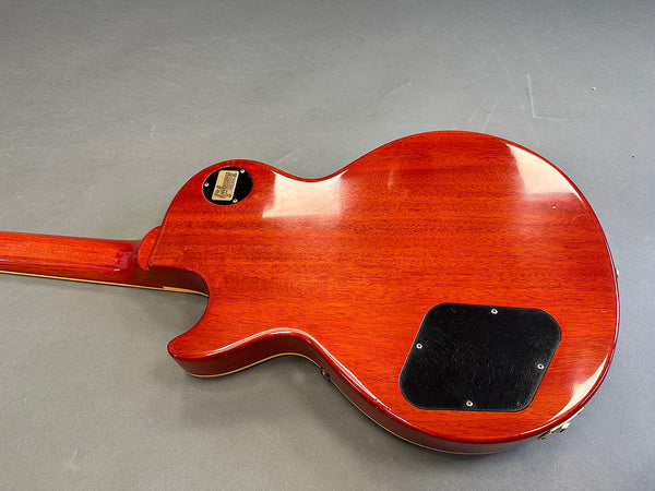 Back view of Cherry red Gibson Les Paul electric guitar showing wood grain and control cavity cover plate on gray surface