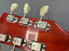 Close-up of vintage-style guitar tuning pegs with cream-colored buttons on reddish-brown wooden guitar headstock, showing metal machine heads with screws.