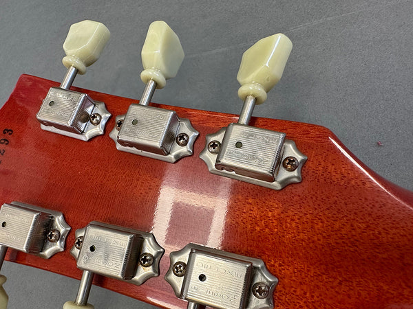 Close-up of vintage-style guitar tuning pegs with cream-colored buttons on reddish-brown wooden guitar headstock, showing metal machine heads with screws.