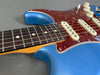 Close-up of blue electric guitar body with tortoiseshell pickguard and rosewood fretboard showing six strings and white dot inlays