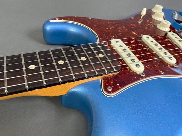 Close-up of blue electric guitar body with tortoiseshell pickguard and rosewood fretboard showing six strings and white dot inlays