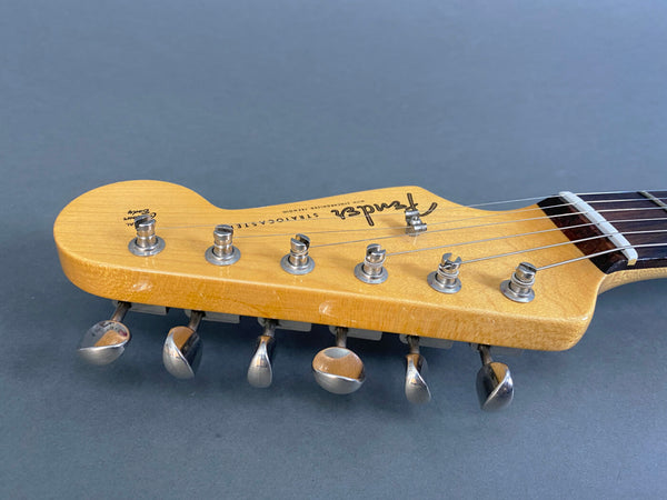 Close-up view of Fender Stratocaster guitar headstock with six tuning pegs and strings on gray background