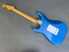 Electric guitar with blue body and natural wood neck shown from the back on a gray background