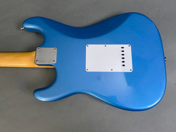 Back view of electric guitar with blue body, white backplate, and natural wood neck and metal neck plate on gray background
